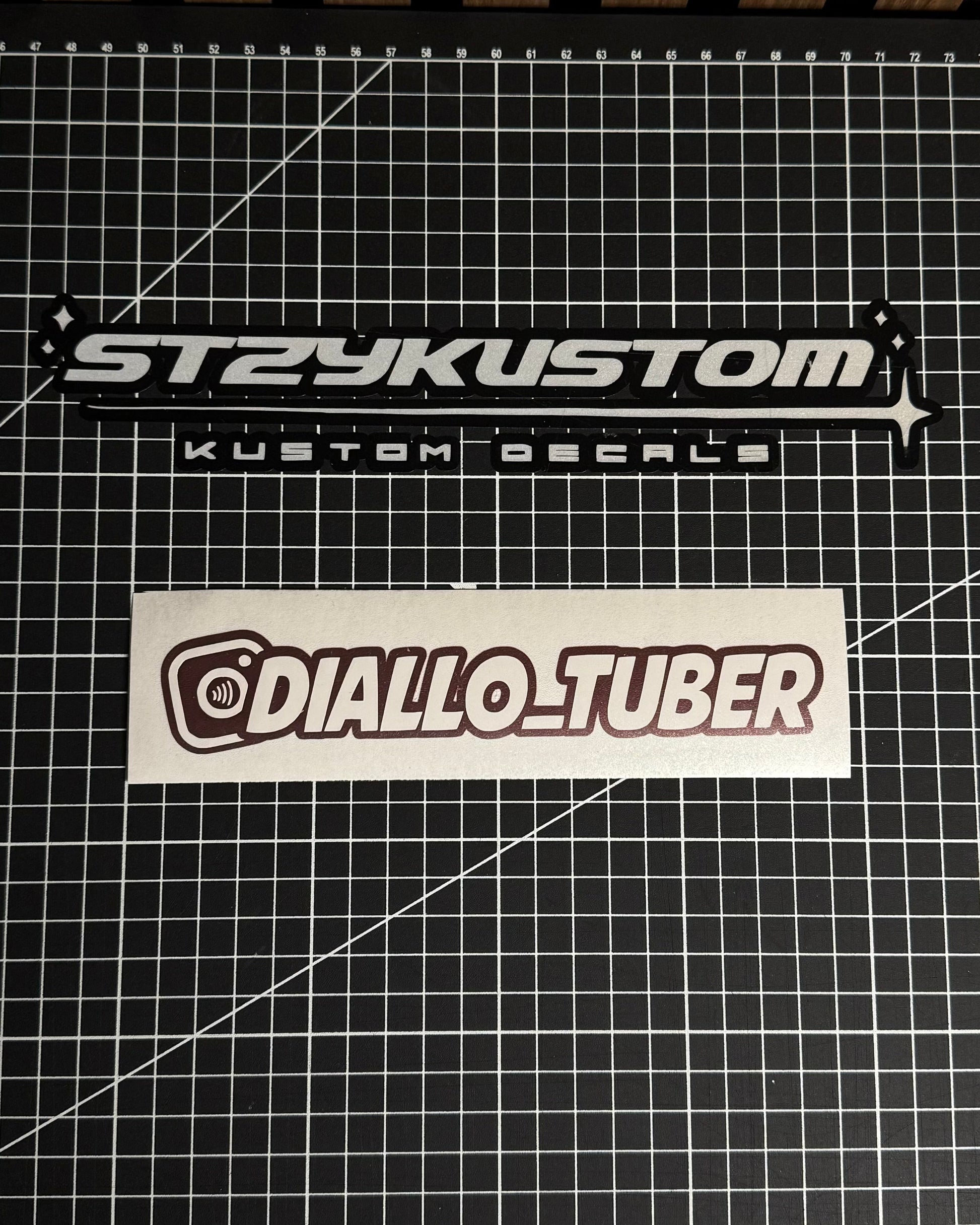 Two stickers on a grid surface, one labeled 'STRYKUSTOM' and the other 'DIALLO_TUBER'.