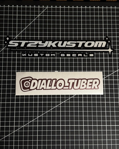 Two stickers on a grid surface, one labeled 'STRYKUSTOM' and the other 'DIALLO_TUBER'.