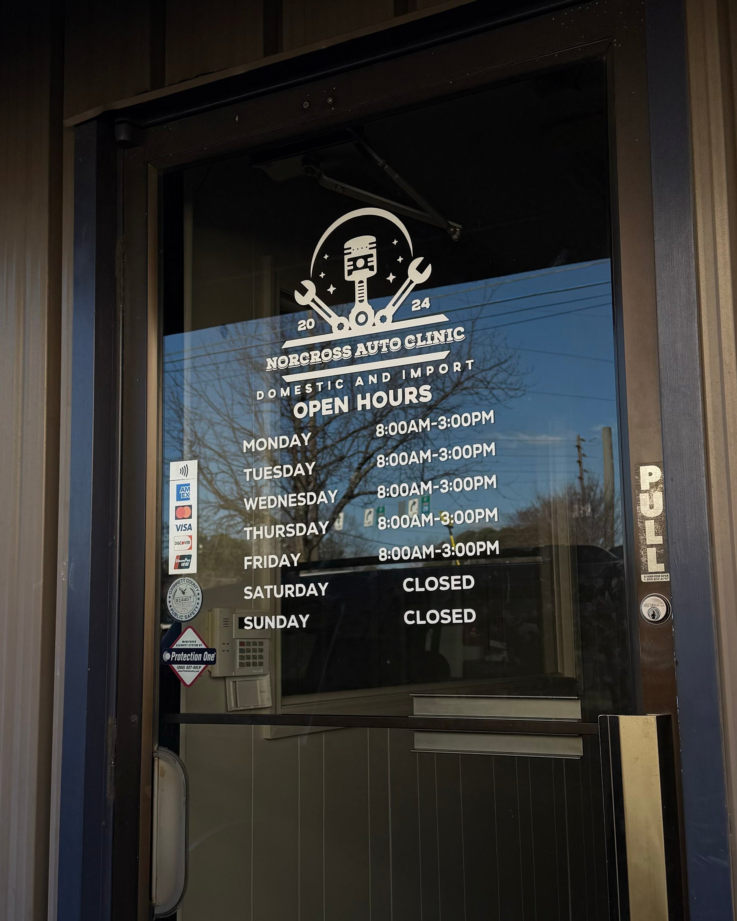Electronic door sign with hours of operation displayed on a glass door.