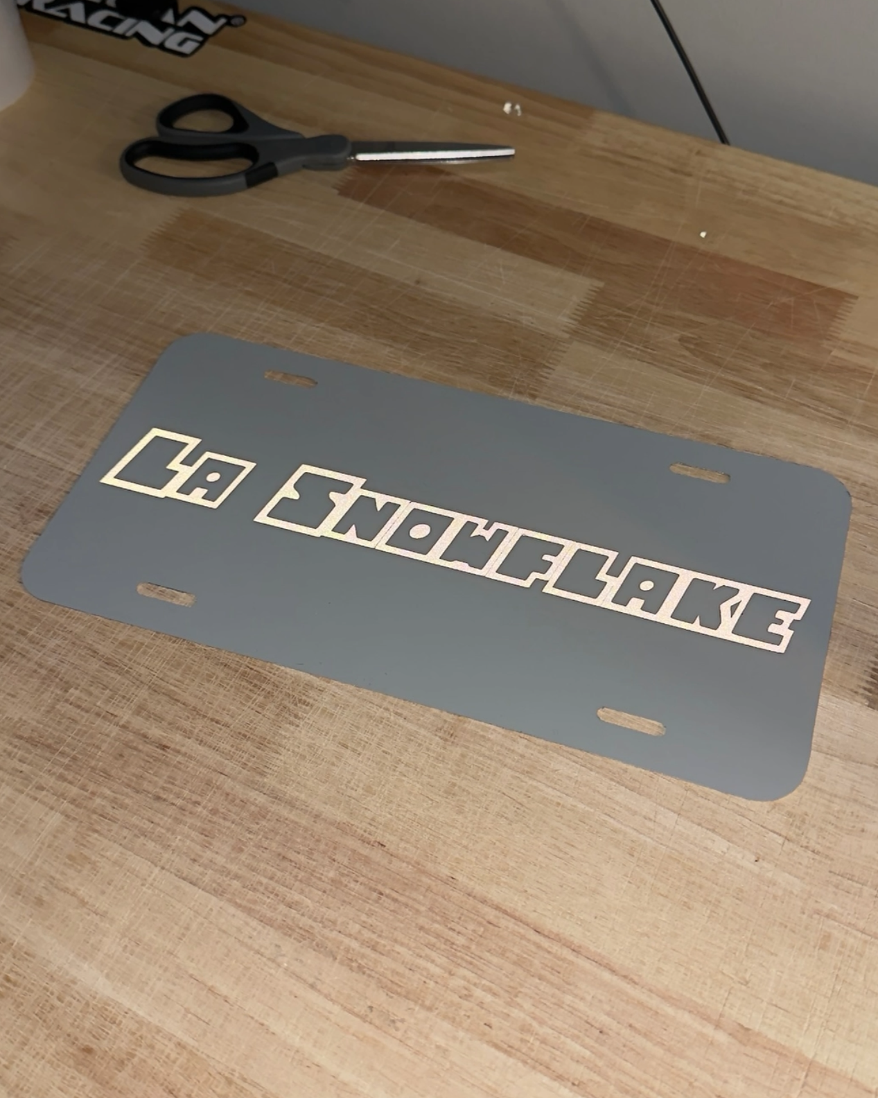 License plate with 'LA Snowflake' text on a wooden surface with scissors.